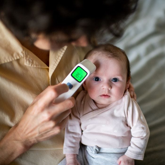 Baby sat upright on parent’s lap supported with hand with thermometer being held to their head.