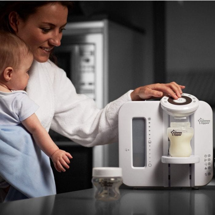 Mother-in-kitchen-with-her-baby-in-her-arms-using-the-Perfect-Prep-machine-to-prepare-a-bottle-of-formula-milk
