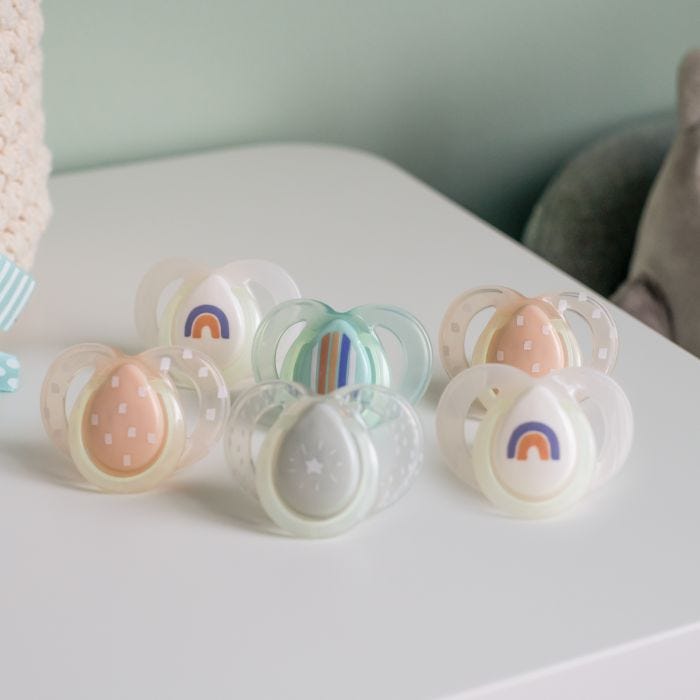 5 Night-Time soothers in various colours and designs on a white table.