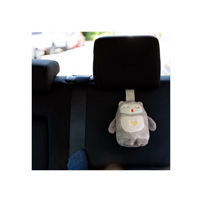 Ollie the Owl Travel Sleep Aid hanging from the headrest of a black car seat