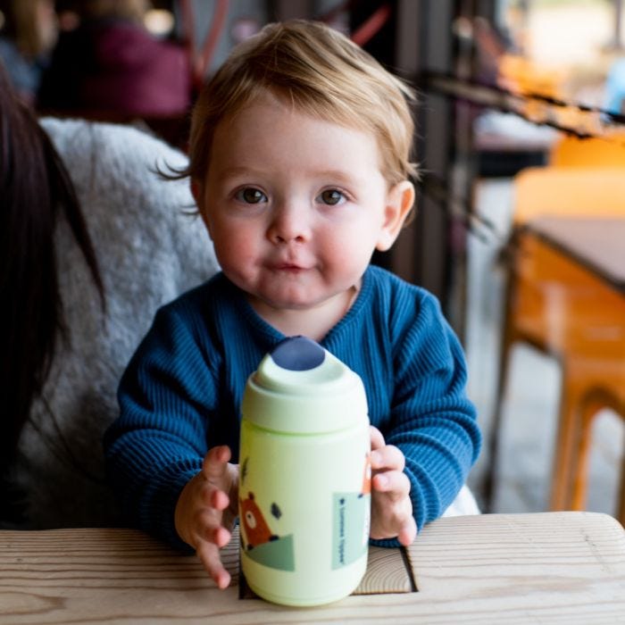 Toddler holding Superstar Sipper Training Cup, green on tabletop