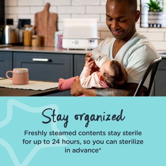 Dad feeding baby in kitchen with white steam sterilizer in the background and text about staying organized
