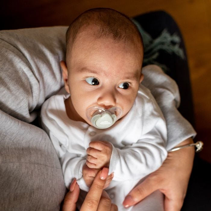 Baby with Night-Time pacifier in mouth being cradled in mom’s arms.