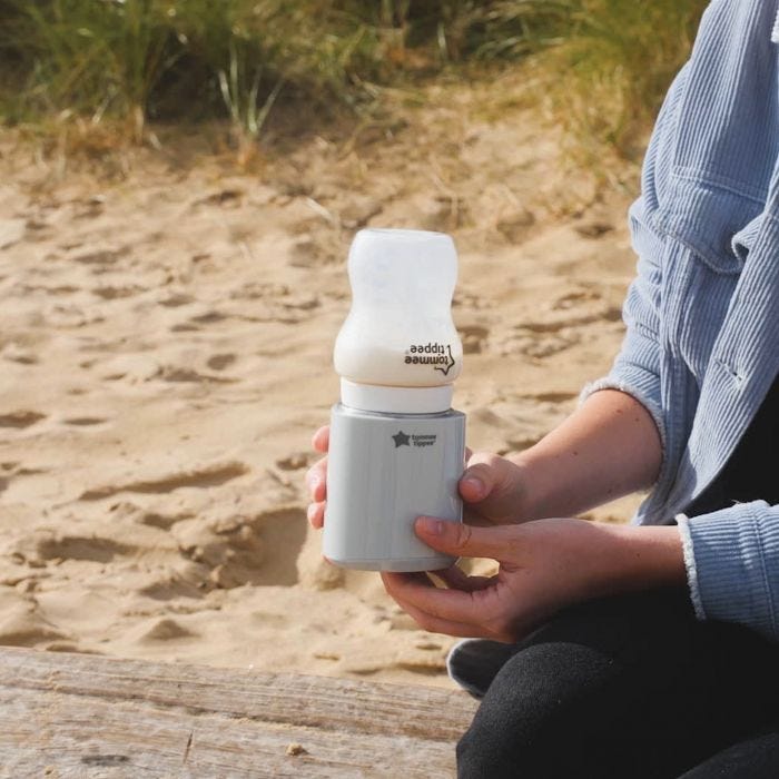Woman holding LetsGo bottle warmer with upside down baby bottle on top while at the beach