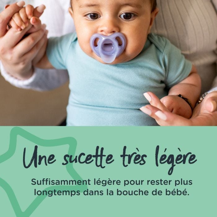 Bébé assis avec la sucette dans la bouche en tenant la main de ses parents.