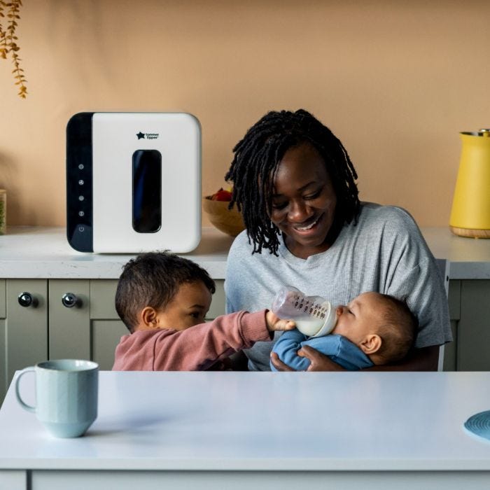 Mum feeding baby in kitchen with white UV steriliser behind her