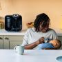 Mother feeding baby in the kitchen with the Perfect Prep machine behind her