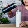 Femme assise dehors versant de l&apos;eau bouillante du thermos à eau chaude dans le thermos refroidisseur
