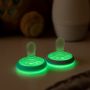Two breast-like night soothers glowing in the dark on a white table.