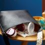 Handbag lying flat on a table with a breast pump and nipple cream peeping out