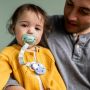 Child sitting on dad’s knee with a soother in mouth attached to the soother holder with a purple clip.