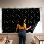 Woman in a yellow t-shirt fixing the portable blackout blind to a window in a baby&apos;s room.