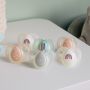 5 Night-Time soothers in various colours and designs on a white table.