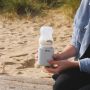 Woman holding LetsGo bottle warmer with upside down baby bottle on top while at the beach