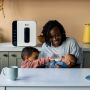 Mum feeding baby in kitchen with white UV steriliser behind her