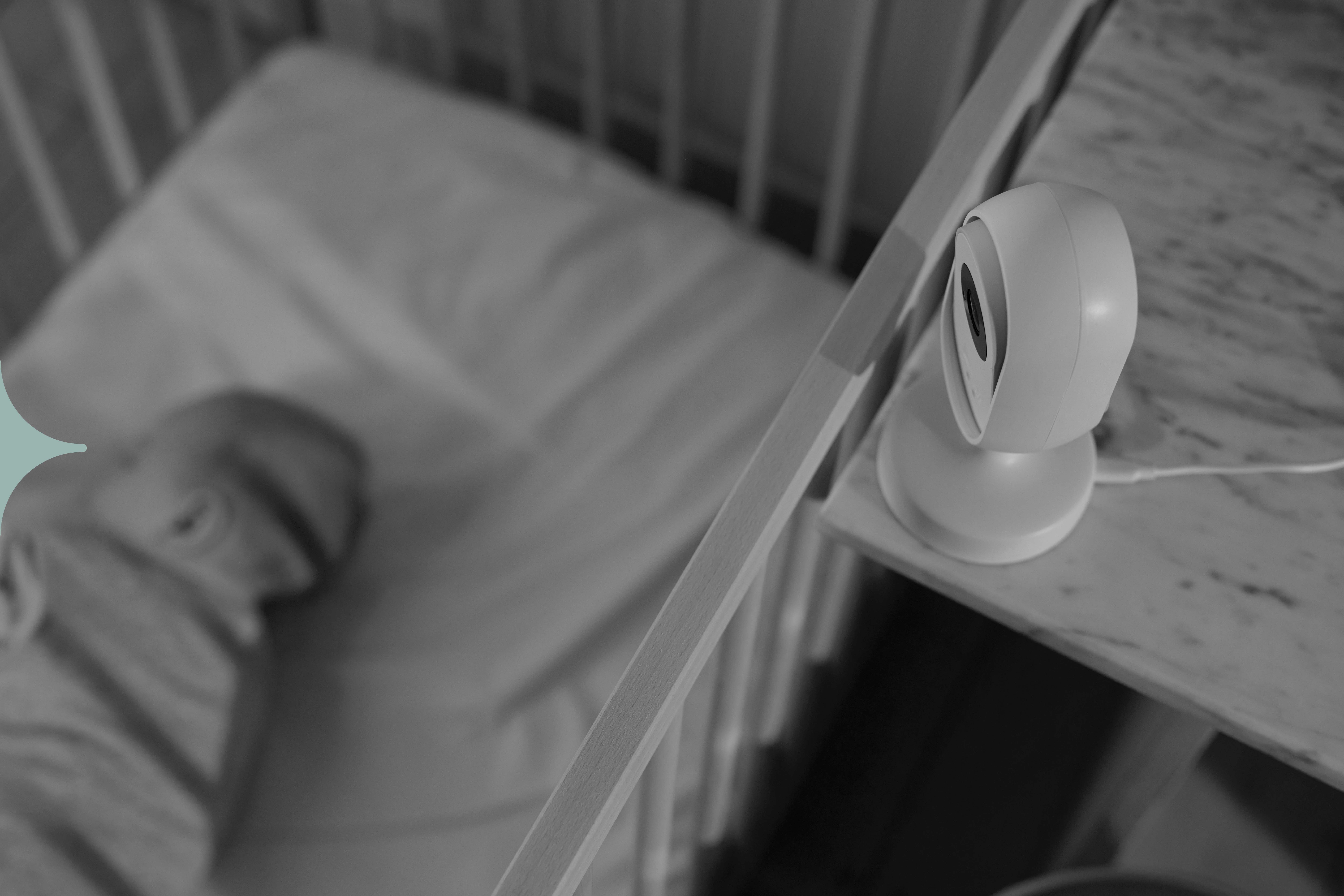 A black and white photo of a baby sleeping in their cot. They're being watched by a sleep monitor.