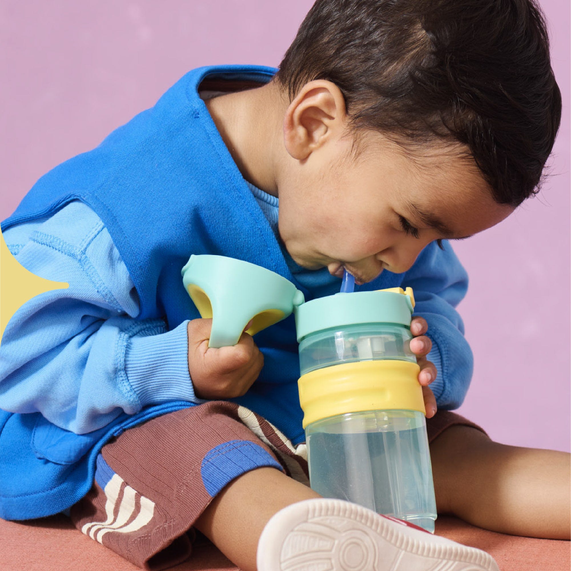  Image shows a child drinking from a purple Tommee Tippee On-the-Go Straw cup (assisted by their mother).