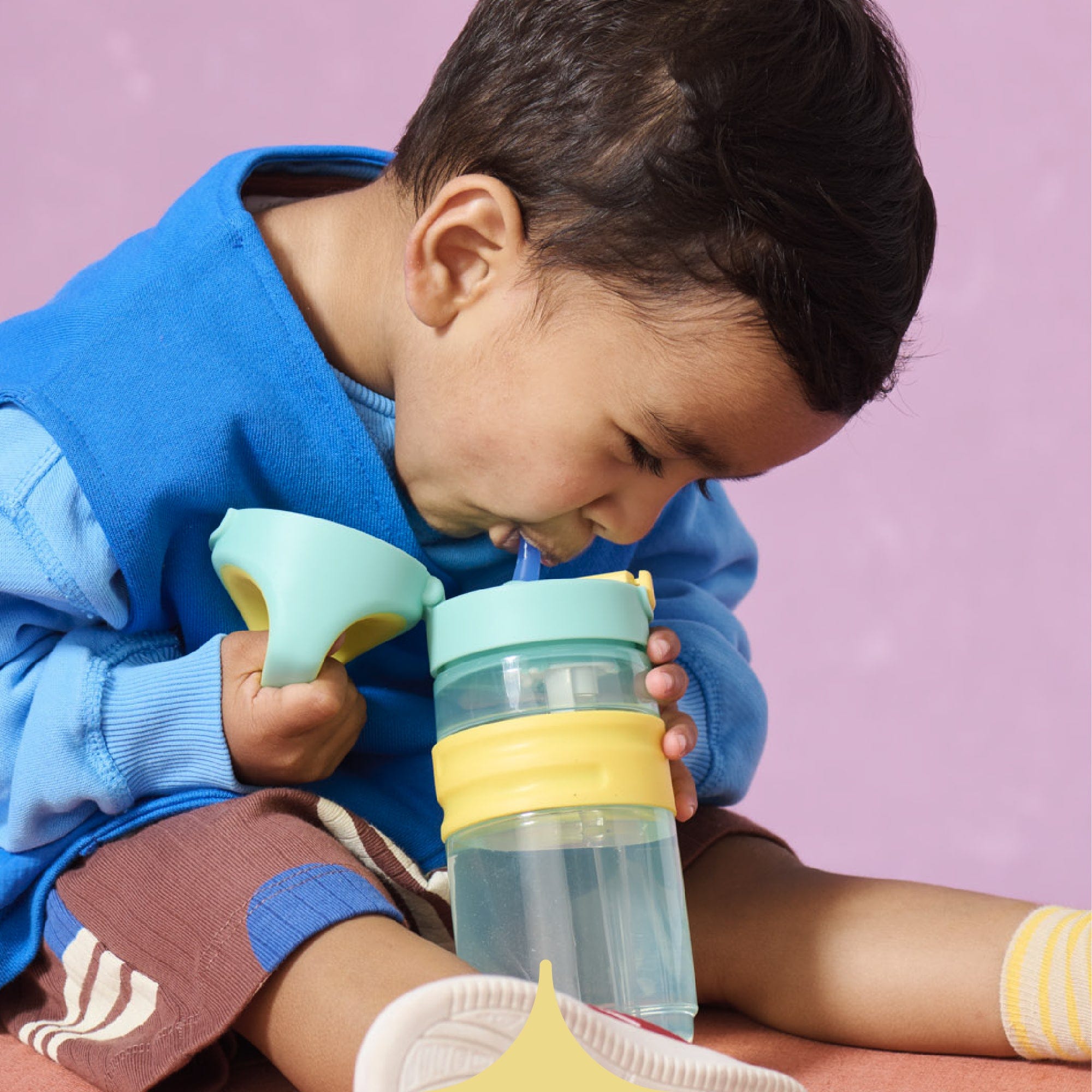  Image shows a child drinking from a purple Tommee Tippee On-the-Go Straw cup (assisted by their mother).