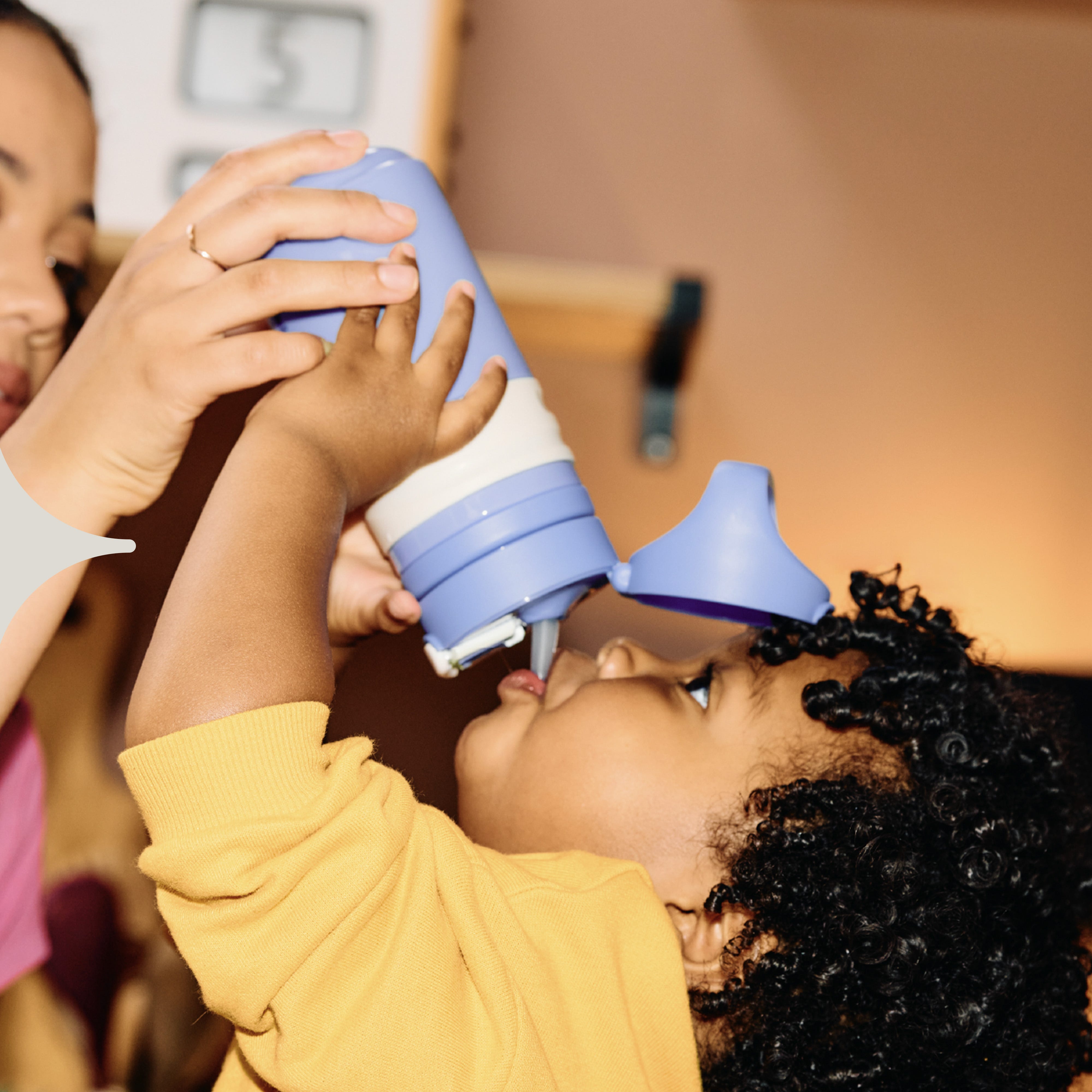  Image shows a child drinking from a purple Tommee Tippee On-the-Go Straw cup (assisted by their mother).