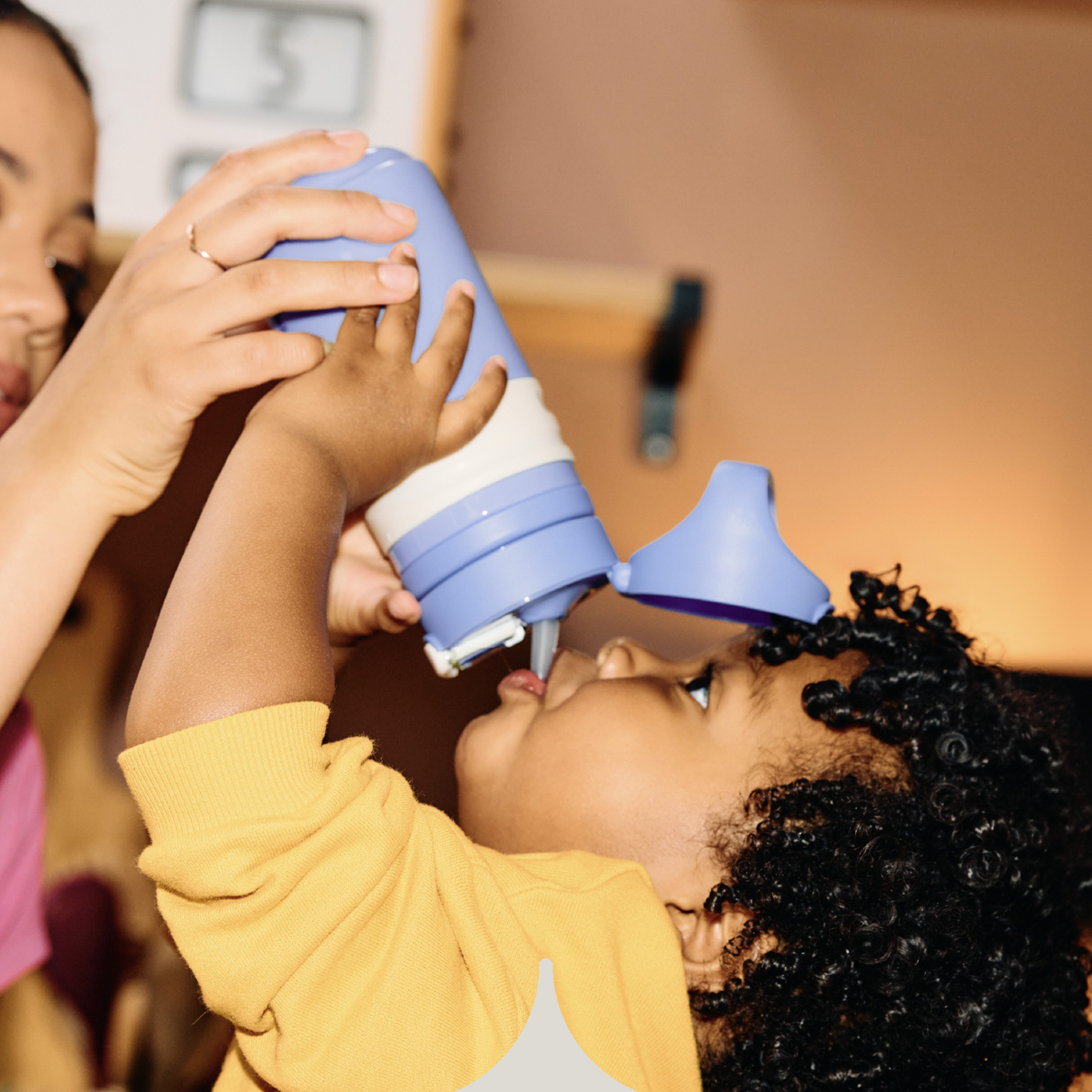  Image shows a child drinking from a purple Tommee Tippee On-the-Go Straw cup (assisted by their mother).
