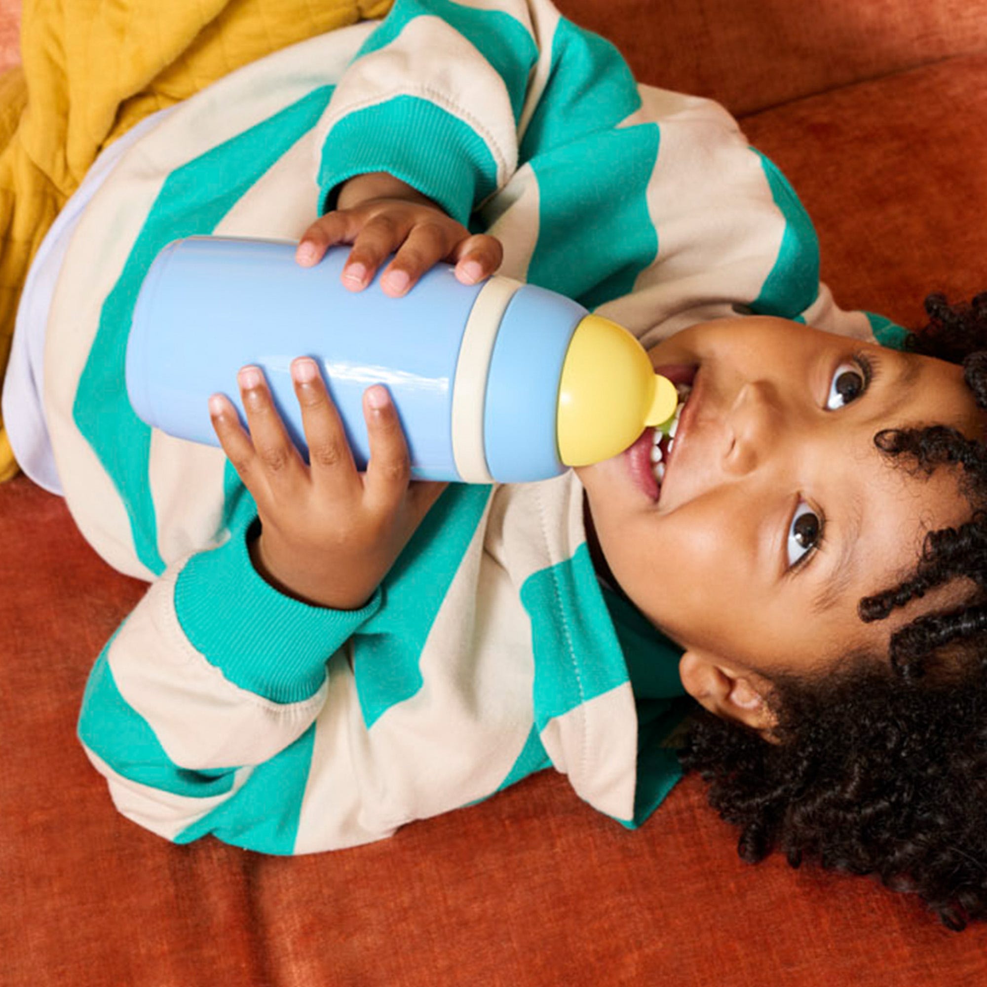  Image shows a child drinking from a purple Tommee Tippee On-the-Go Straw cup (assisted by their mother).