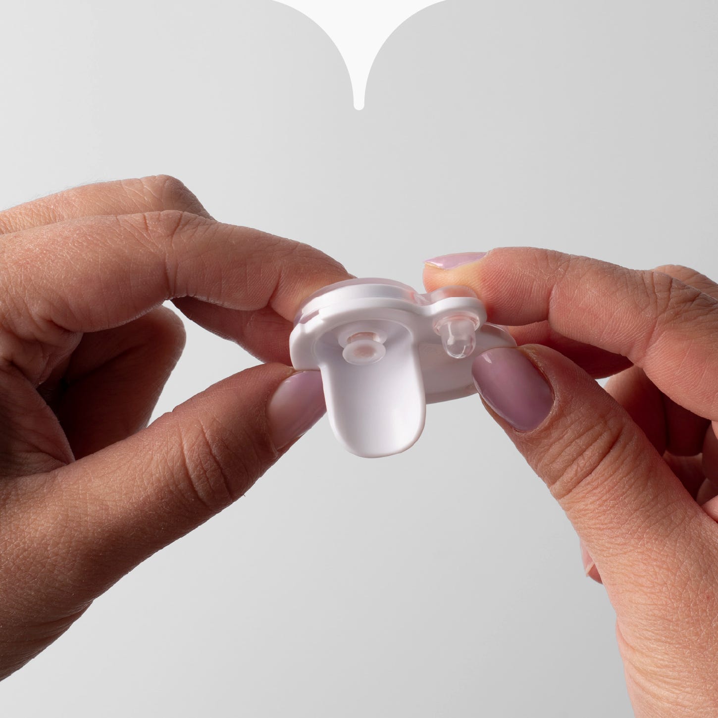 Close up image of hands attaching the pieces of a Tommee Tippee spout cup valve, together. 